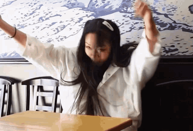 a woman is sitting at a table with her arms outstretched
