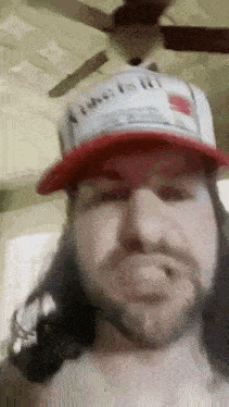 a man with long hair and a beard is wearing a red hat and a ceiling fan .
