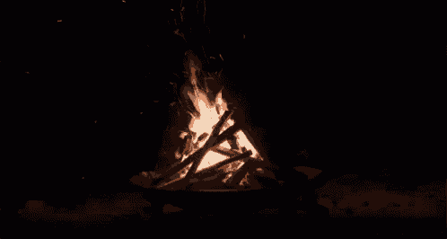 a campfire is burning in the dark with sparks coming out of it .