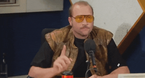 a man with a mustache wearing sunglasses and a leather vest is giving a thumbs up