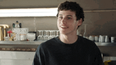 a young man in a black shirt is smiling in front of a shelf full of glasses