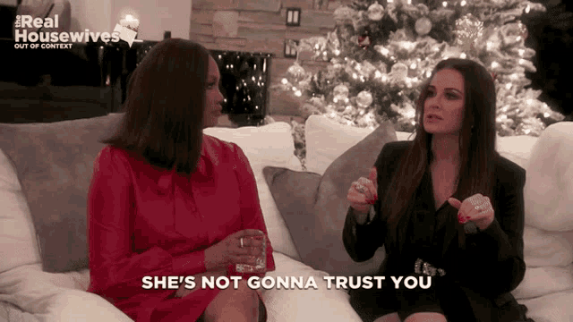 two women are sitting on a couch with the words she 's not gonna trust you