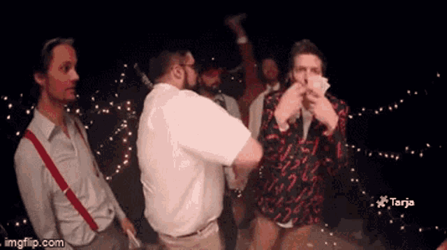 a group of men are dancing and one of them is holding a stack of money in his hand