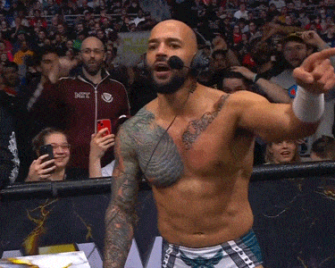 a shirtless wrestler wearing headphones holds up a sign that says " i 'm a fighter "