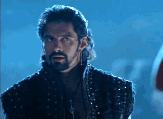 a man with long hair and a beard is wearing a black vest