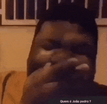 a man with a beard is covering his mouth with his hands while talking on a video call .