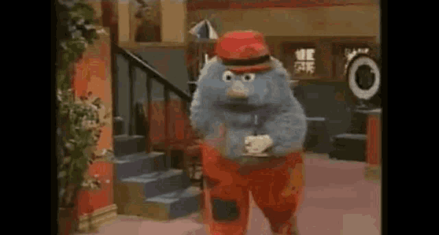 a stuffed animal wearing a hat and patched pants is standing in a room .