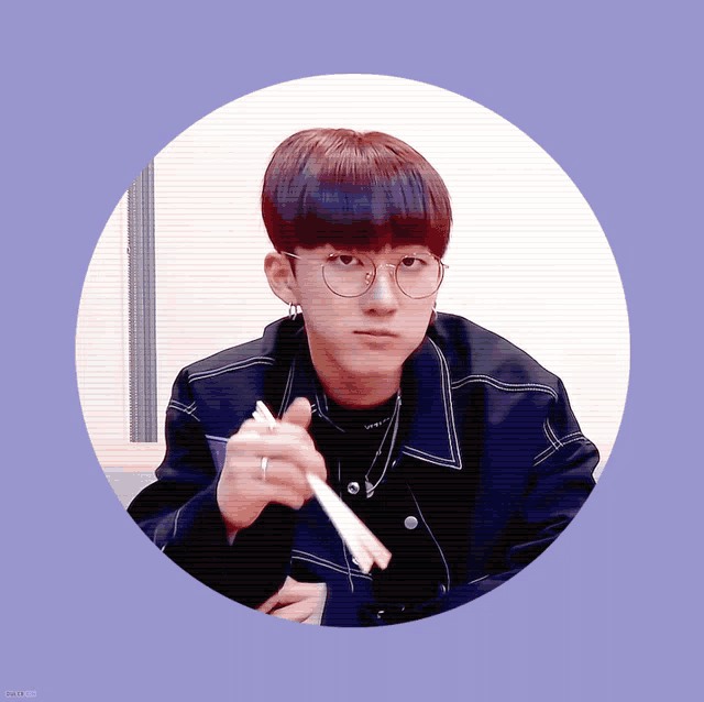 a young man wearing glasses and a black jacket is holding chopsticks