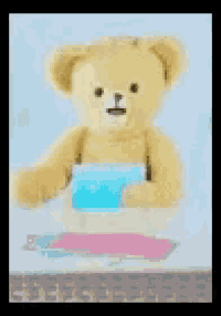 a teddy bear is sitting at a table with a pink and blue blanket on it .