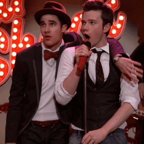 a man singing into a microphone while another man stands behind him