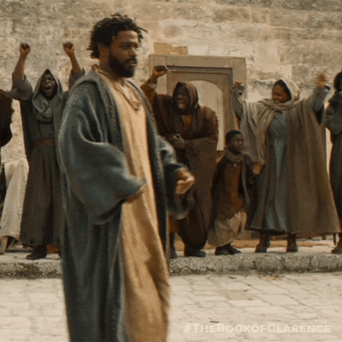 a man in a robe stands in front of a group of people with their hands in the air