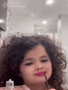 a young girl with curly hair is applying pink lipstick to her lips .