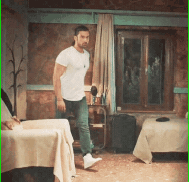 a man in a white t-shirt is standing in a room with two beds