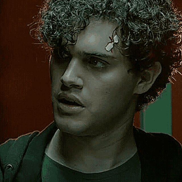 a man with curly hair and a bandage on his forehead is looking at the camera .