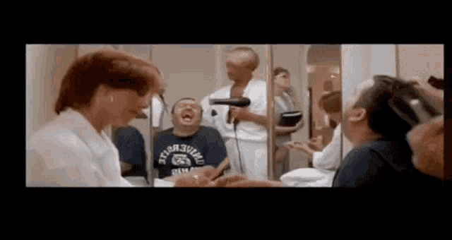 a group of people are sitting in front of a mirror getting their hair blow dried by a woman .