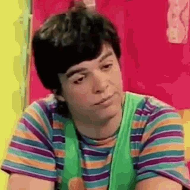 a young man wearing a striped shirt and a green vest is making a sad face .