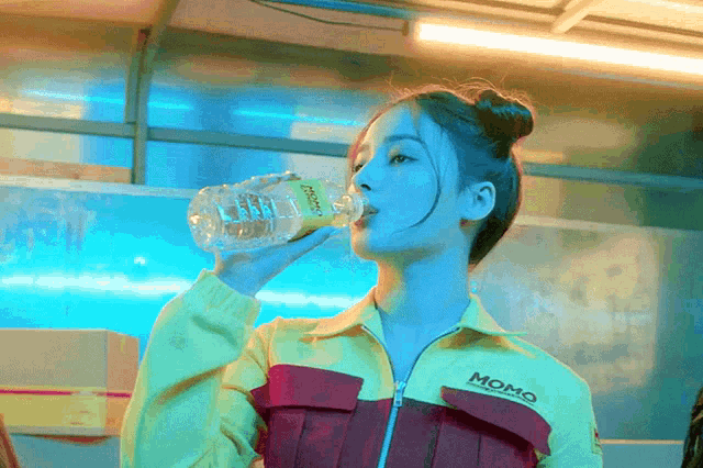 a woman wearing a yellow momo jacket drinks from a bottle
