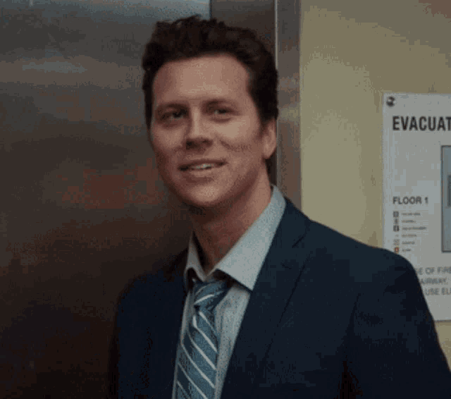 a man in a suit and tie is smiling in front of an evacuation sign on the wall