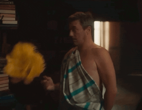 a shirtless man wrapped in a striped towel is standing in a dark room .