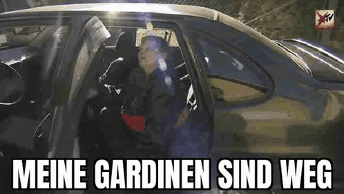 a man is sitting in a car with the words meine gardinen sind weg written above him .
