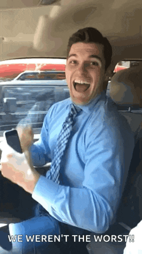 a man in a blue shirt and tie is sitting in the back seat of a car holding a cellphone .