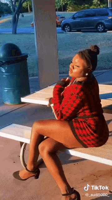 a woman in a red dress is sitting on a bench with her legs crossed .
