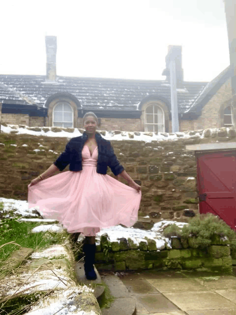a woman in a pink dress stands in front of a snowy building