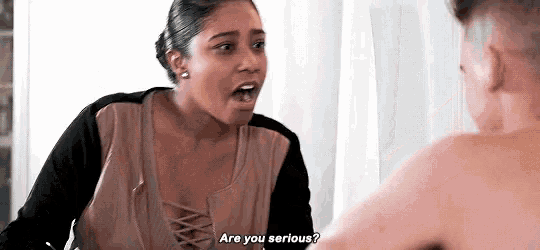 a woman is talking to a shirtless man in front of a mirror and asking him if he is serious .