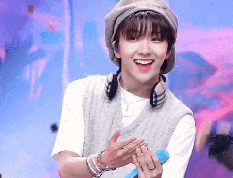 a young man wearing a hat and a vest is smiling and clapping