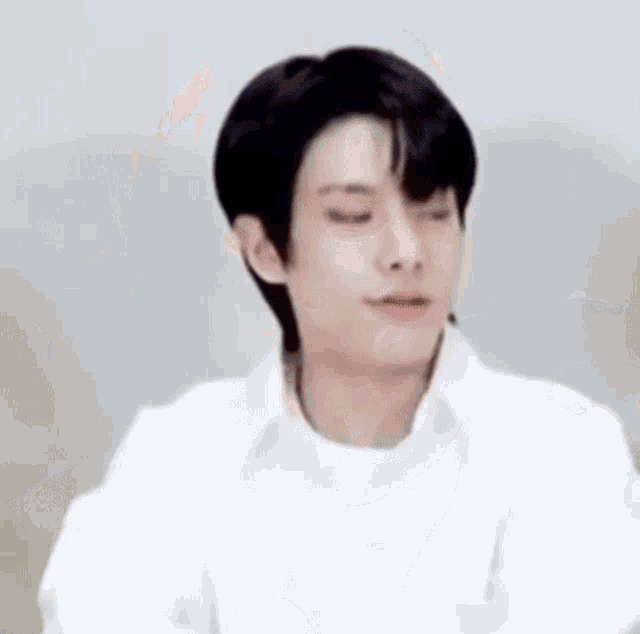 a young man wearing a white shirt and black hair is making a funny face .