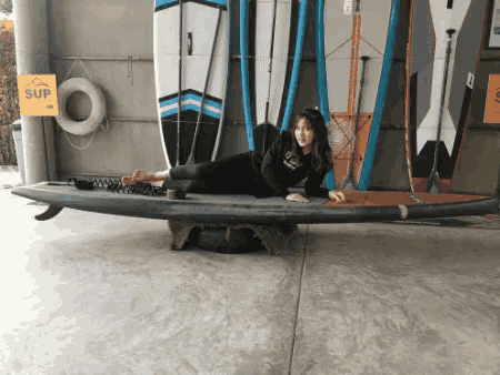 a woman laying on a surfboard in front of a yellow sign that says sup