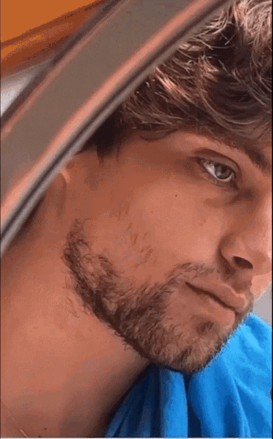 a close up of a man 's face with a beard and blue shirt