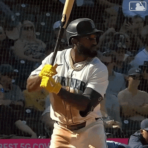 a baseball player wearing a mariners jersey is swinging a bat