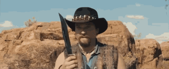 a man in a cowboy hat is holding a large knife in his hand