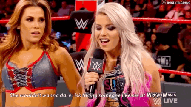 two women are standing next to each other in a wrestling ring talking into microphones .