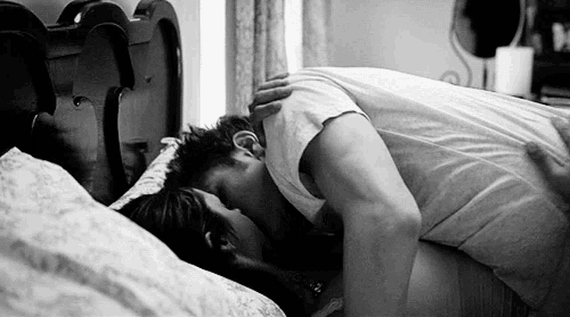 a man and a woman are kissing on a bed in a black and white photo .