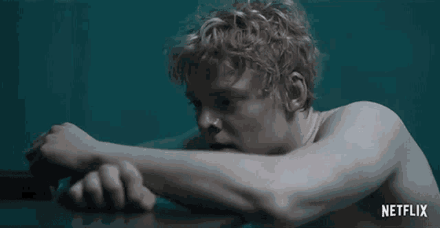 a shirtless man with curly hair is laying on a table with his head on his elbow .