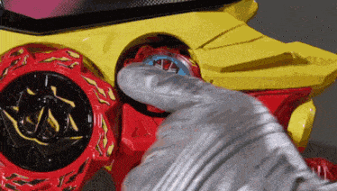 a person wearing a silver glove is holding a red and yellow toy car in their hand .