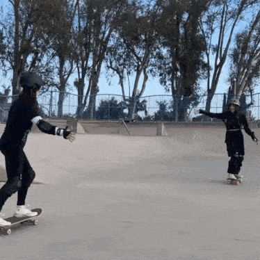 two women are riding skateboards in a skate park with trees in the background