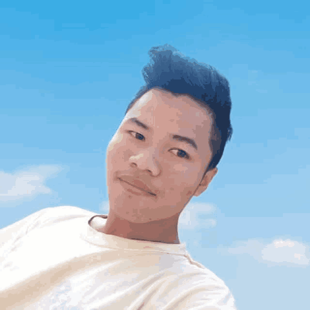 a young man is taking a selfie with a blue sky behind him .