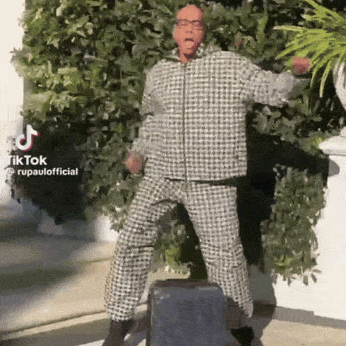 a man in a plaid suit is jumping in the air with a suitcase behind him .