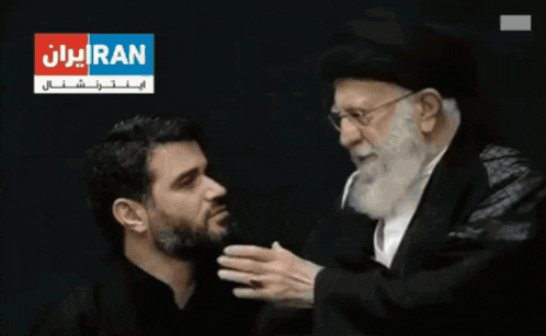 a man is touching another man 's neck in front of a sign that says iran on it