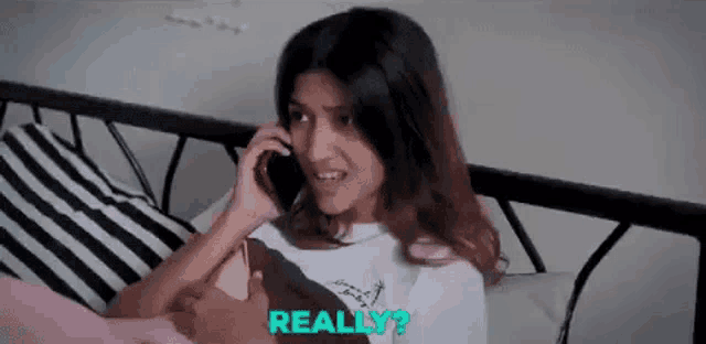 a woman is lying on a bed talking on a cell phone .