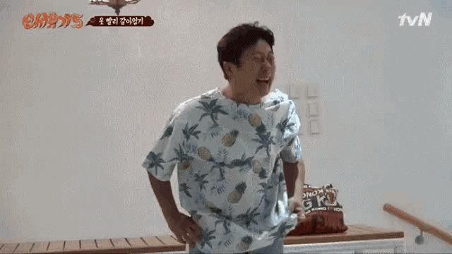 a man in a hawaiian shirt is laughing while standing in front of a table .