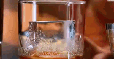 a glass of whiskey is being poured into a glass filled with ice .