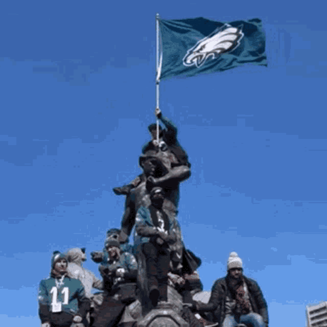 a group of people standing on top of a statue holding a flag with the eagles logo on it