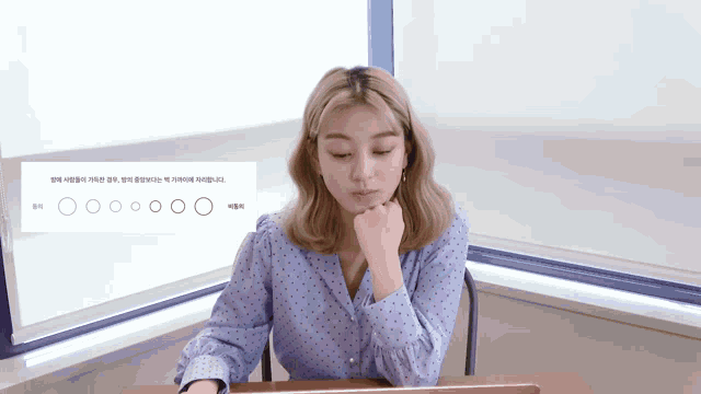 a woman is sitting at a desk with a sign behind her that says ' o ' on it