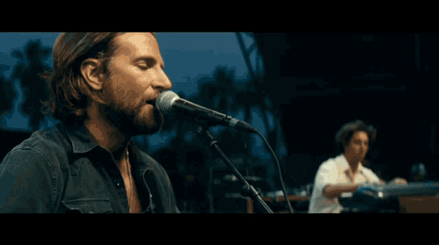 a man singing into a microphone while another man plays a piano