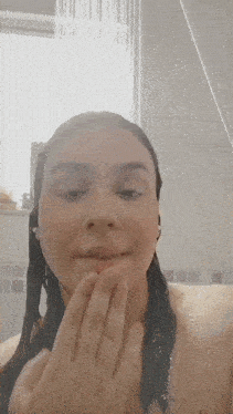 a woman is taking a shower and touching her face with her hand .