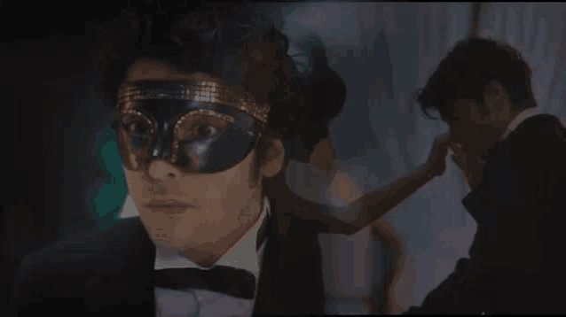 a man in a tuxedo and mask is standing next to a woman in a dress .